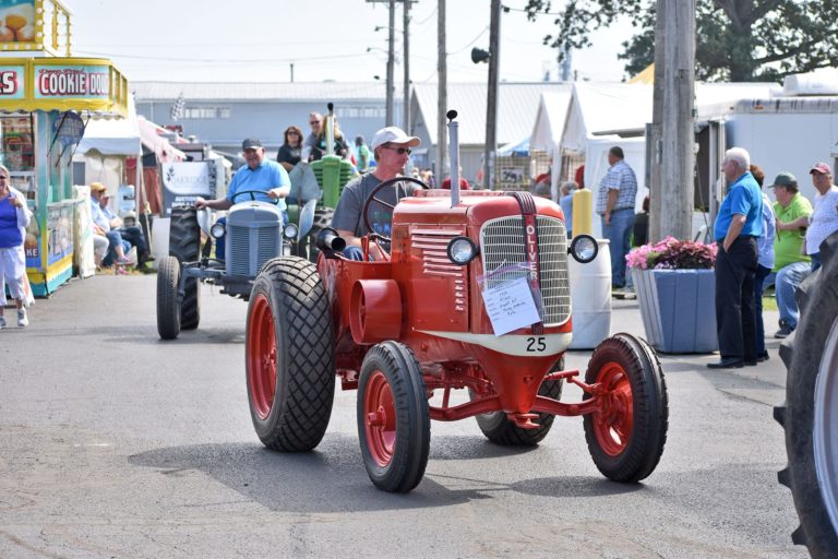 A man driving a red antique tractor through the fairgrounds for a parade.